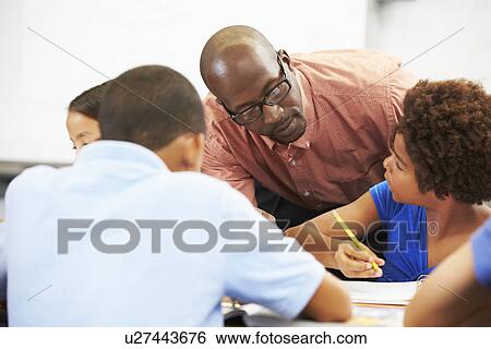 Teacher Helping Pupils Studying At Desks In Classroom View Large Photo Image Stock Photograph - Teacher Helping Pupils Studying At Desks In Classroom. Fotosearch
