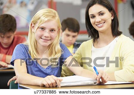 Stock Photography - Teacher Helping Pupils Studying At Desks In Classroom. Fotosearch