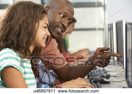 Stock Image - Teacher Helping Students Working At Computers In Classroom. Fotosearch