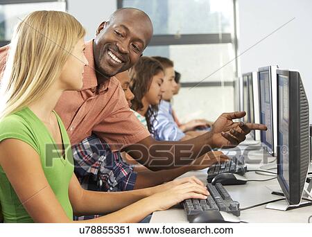 Stock Image - Teacher Helping Students Working At Computers In Classroom. Fotosearch