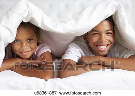 Stock Photo - Two Children Hiding Under Duvet In Bed. Fotosearch