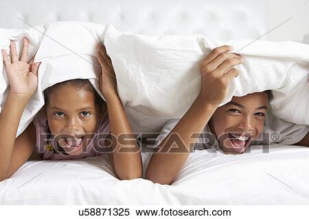 Stock Photography - Two Children Hiding Under Duvet In Bed. Fotosearch