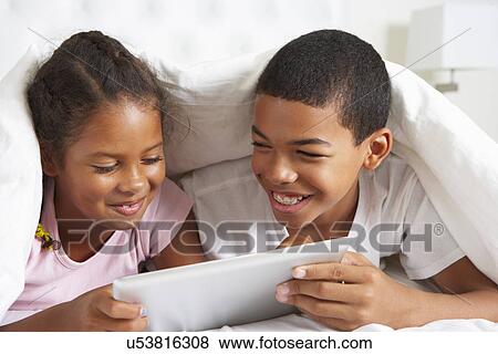 Stock Photo - Two Children Using Digital Tablet Under Duvet. Fotosearch