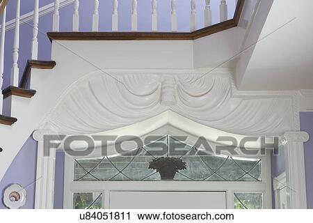Stock Image - Architectural detail: View of top section of passageway surround. Pilasters and columns. Stairway crosses over entryway. White woodwork and lavender walls.. Fotosearch