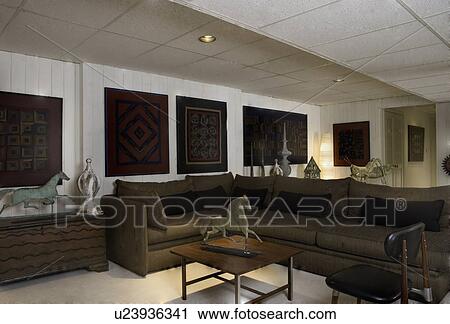 BASEMENT LIVING: family room area, Amish quilts line the walls, antique weathervanes, and architectural salvage finials, dark brown sectional sofa, black pillows, mid century modern table and chair View Large Photo Image Stock Image - BASEMENT LIVING: family room area, Amish quilts line the walls, antique weathervanes, and architectural salvage finials, dark brown sectional sofa, black pillows, mid century modern table and chair. Fotosearch