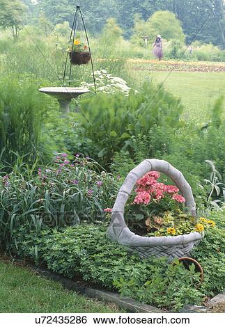 Stock Photograph - Basket of flowers and birdbath in garden. Fotosearch