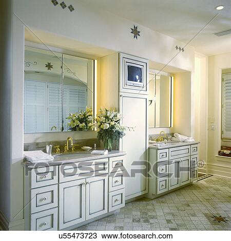 Stock Image - BATHROOM - Cream cupboards, two sink areas, television, tile floor, southwestern designs, floral arrangement,. Fotosearch