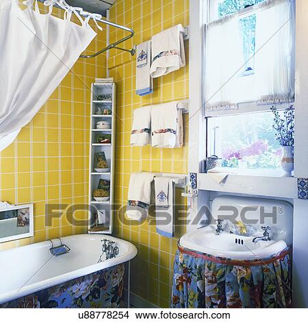 Picture - BATHROOMS: Blue and pink floral skirt on sink on right. Small floral pattern on base of tub on left. Yellow ceramic tile walls above tub.. Fotosearch