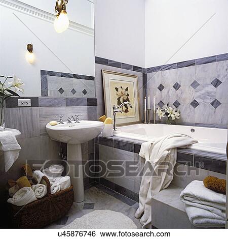 BATHROOMS: Contemporary. Marble tile in shades of grey. View towards pedestal sink with large mirror above with sconce. Wicker basket under sink holds extra white towels and scrubs. Bath tub on right. Framed art of white flower. View Large Photo Image Stock Photograph - BATHROOMS: Contemporary. Marble tile in shades of grey. View towards pedestal sink with large mirror above with sconce. Wicker basket under sink holds extra white towels and scrubs. Bath tub on right. Framed art of white flower.. Fotosearch