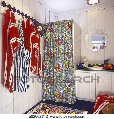 Stock Image - BATHROOMS: Pool house. Shower stall with very busy red, yellow, green, and blue floral tiny pattern curtain. Tiny sink area on right with green countertop and rubber ducks. Red, white and green and white striped cotton robes and linens hanging on rack on . Fotosearch