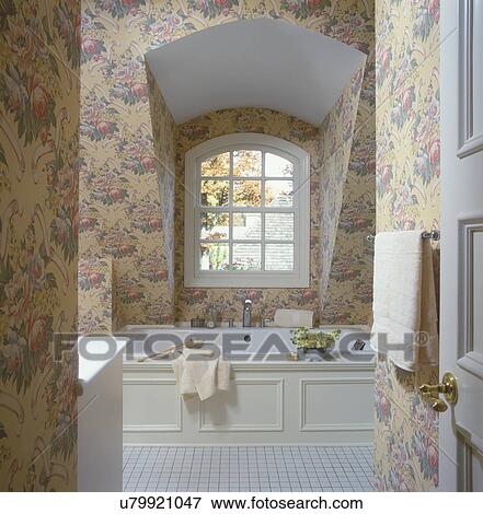 BATHROOMS - Upstairs bath, tub under dormer window, large floral print wallpaper in pale yellow, greens and pink blooms, Tile floor, paneled tub surround View Large Photo Image Stock Photo - BATHROOMS - Upstairs bath, tub under dormer window, large floral print wallpaper in pale yellow, greens and pink blooms, Tile floor, paneled tub surround. Fotosearch