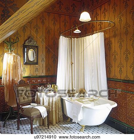 BATHROOMS: Victorian, deep tub, gilded claw feet, glazed Spanish tile dado, 'Emperor' wallpaper, upholstered chair, old style brass shower, tile floor, pendant lighting View Large Photo Image Stock Image - BATHROOMS: Victorian, deep tub, gilded claw feet, glazed Spanish tile dado, 'Emperor' wallpaper, upholstered chair, old style brass shower, tile floor, pendant lighting. Fotosearch
