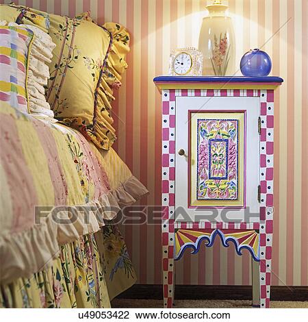Stock Image - BEDROOMS: Detail of colorful hand painted nightstand in children's bedroom. Striped wallpaper and floral bed sheets. . Fotosearch