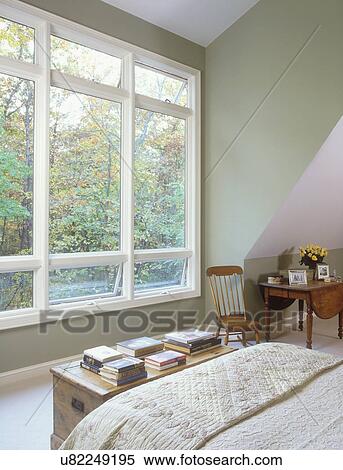 Stock Photography - BEDROOMS: Grey-green hue on walls, large white nine foot windows, no curtains, view of woods in fall. Chest at foot of bed with lots of books on top.. Fotosearch