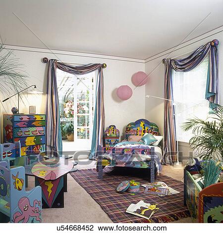 Stock Image - CHILDREN'S BEDROOM: Hand decorated furniture in primary colors, colorful striped window swags, area rug on pale pink square.. Fotosearch