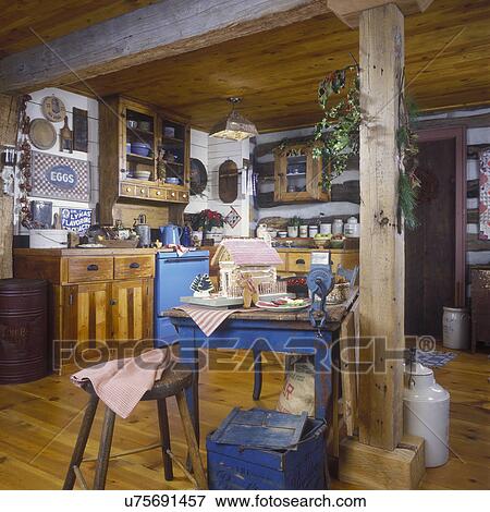 Stock Photo - CHRISTMAS INTERIORS - Rustic country kitchen ready for the holidays, blue table with Gingerbread house. Wooden floors, trade signs on wall.. Fotosearch