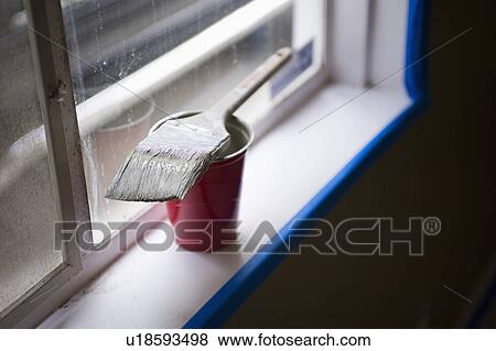 Stock Photo - Close-up of paint brush resting on red plastic glass on window sill. Fotosearch