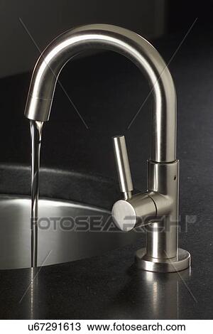 Stock Image - Close-up of stainless steel faucet with falling water in sink on kitchen counter. Fotosearch