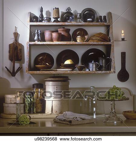 Stock Photo - COLLECTION DISPLAY - Antique wall shelf with antique pewter, red ware etc., displayed in a modern Early American style kitchen.. Fotosearch
