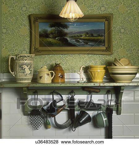 Stock Photo - COLLECTION DISPLAY - Detail of antique wall shelf above sink with 19th century kitchen utensils and pottery, etc. 1880's repro wallpaper pattern. Classic subway tile.. Fotosearch