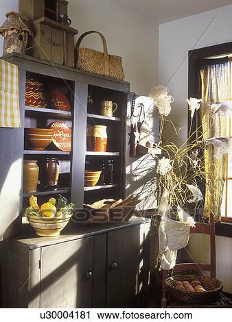 Stock Image - COLLECTION DISPLAY- Red ware, slipware pottery displayed on shelves of antique painted farm cupboard, fall pampass grass, gourds in yellow ware bowl, baskets, modern country, simple, clean, nostalgic. Fotosearch