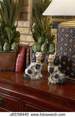 Stock Image - COLLECTION DISPLAY two Chelsea style ceramic dogs, lamp base, books, dried floral arrangement. Fotosearch