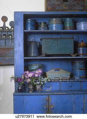 Stock Image - COLLECTION DISPLAYS - American blue primitive weathered cupboard, blue and teal firkins, Shaker and pantry boxes. Purple and violet flowers detail still life shot . Fotosearch