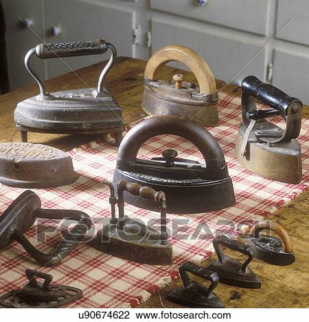 Stock Image - COLLECTION DISPLAYS - Antique irons on woven checkerboard table runner. . Fotosearch