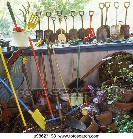Stock Photo - COLLECTION DISPLAYS - Miniature garden tools, shovels and spades of all sizes, folk art painted rooster, vintage farm toys, tractors and chickens, terra cotta pots and potting soil. Fotosearch