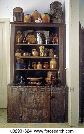 Picture - COLLECTION DISPLAYS: Primitive dark cabinet holds collection of brown ware pottery and Early American wooden boxes, slipware, figural pottery . Fotosearch