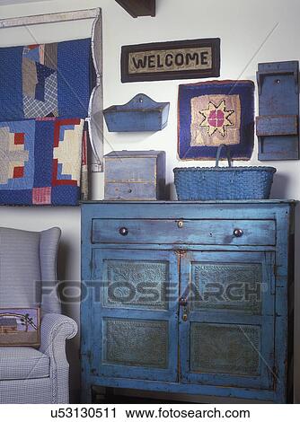 COLLECTION DISPLAYS - Welcome rug and a small hooked star rug hang amid Primitive wooden boxes, quilts, punched tin paneled blue pie safe, blue and white wing chair. View Large Photo Image Stock Image - COLLECTION DISPLAYS - Welcome rug and a small hooked star rug hang amid Primitive wooden boxes, quilts, punched tin paneled blue pie safe, blue and white wing chair. . Fotosearch