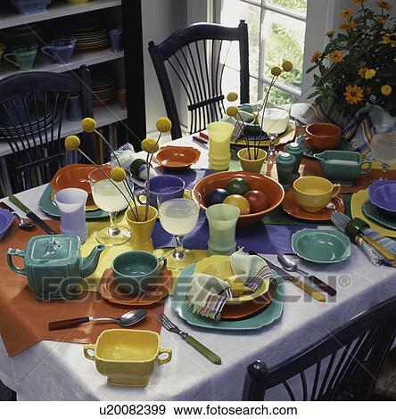 Stock Photo - Colorful table setting in eating area, collection of Riviera ware 1938 - late 40's colors of orange, green, bouquet of flowers by window, Bakelite flatware, chairs. Fotosearch