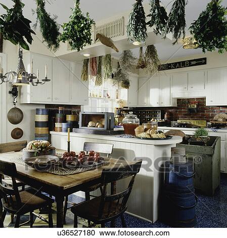 Country kitchen with eating area in forefront, many antiques fruit, herbs and flowers hand from ceiling, painted white pine bowl of apples, pie View Large Photo Image Stock Image - Country kitchen with eating area in forefront, many antiques fruit, herbs and flowers hand from ceiling, painted white pine bowl of apples, pie. Fotosearch