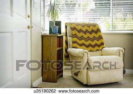Stock Image - Cozy armchair with throw blanket by window in living room, San Diego, California, United States of America. Fotosearch