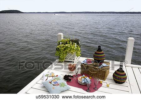 Stock Image - DECK: Overlooking Green Lake, Wi, picnic on pier, colorful dinnerware, basket, planter box at end of pier, horizontal view. Fotosearch