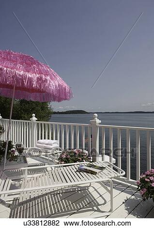 Stock Image - DECK: Overlooking Green Lake, Wi, upper deck, white chaise lounges, pink accents including a pink grass Tiki umbrella. Fotosearch