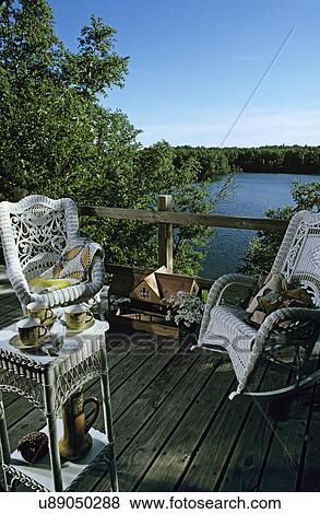 Stock Photo - Decks: Deck of log house at lake. Natural wood. White wicker chair and rocker. Set for tea. . Fotosearch