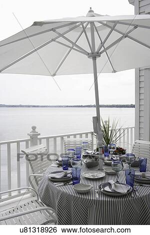 DECKS; Outdoor dining, blue and white place settings, striped ticking tablecloth, white deck, patio furniture and umbrella View Large Photo Image Stock Photograph - DECKS; Outdoor dining, blue and white place settings, striped ticking tablecloth, white deck, patio furniture and umbrella. Fotosearch