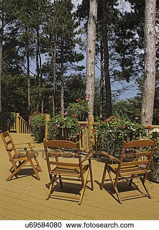 DECKS: Rustic deck with three wood chairs, view towards summer wood with tall pine trees, (lake view), a log railing with planters full of colorful blooming geraniums and vines. View Large Photo Image Stock Image - DECKS: Rustic deck with three wood chairs, view towards summer wood with tall pine trees, (lake view), a log railing with planters full of colorful blooming geraniums and vines. . Fotosearch