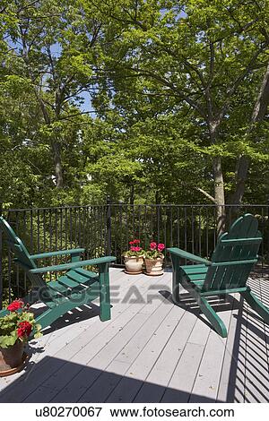 Stock Photo - Decks: Second story deck,, iron railings two green Adirondack chairs look out over canopy of lush green trees. Red geraniums in pots. Fotosearch