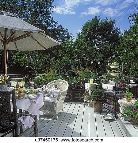 DECKS: Umbrella table on deck, white wicker furniture, set with food, lots of flowers and plants. View Large Photo Image Stock Photography - DECKS: Umbrella table on deck, white wicker furniture, set with food, lots of flowers and plants. . Fotosearch