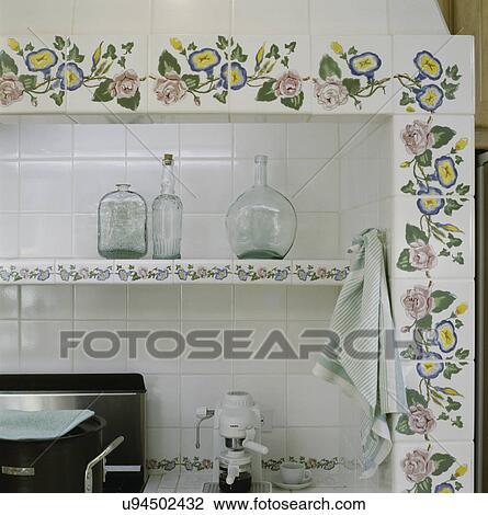 Stock Image - Detail of shelf in alcove stove area, tile back splash and decorative painted flower pattern on border tile. Fotosearch