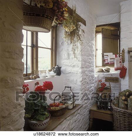 Stock Image - Detail of wooden window seat and white washed brick wall. England, red geraniums, basket of tomatoes, wood, wine in metal carrier, milk carrier, vintage red and white linens, old world, nostalgic. Fotosearch