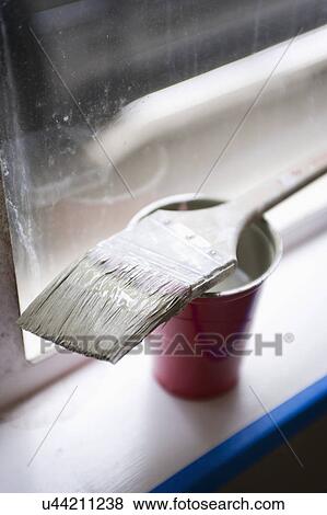 Stock Photo - Detail shot of a paint brush resting on red plastic glass on window sill. Fotosearch