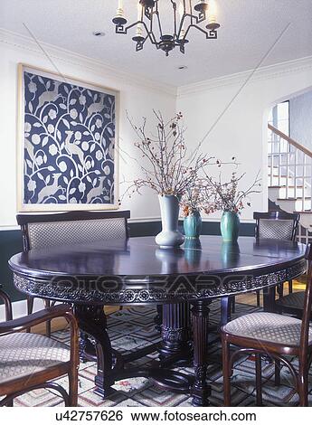 DINING ROOM - Leaping deer wall hanging, ornately carved dark oval dining table with pillar legs, art pottery vases in green, bittersweet branches, bentwood settee and chairs, wood floors, hooked rug, moldings, chair rail, partial chandelier View Large Photo Image Stock Photograph - DINING ROOM - Leaping deer wall hanging, ornately carved dark oval dining table with pillar legs, art pottery vases in green, bittersweet branches, bentwood settee and chairs, wood floors, hooked rug, moldings, chair rail, partial chandelier. Fotosearch