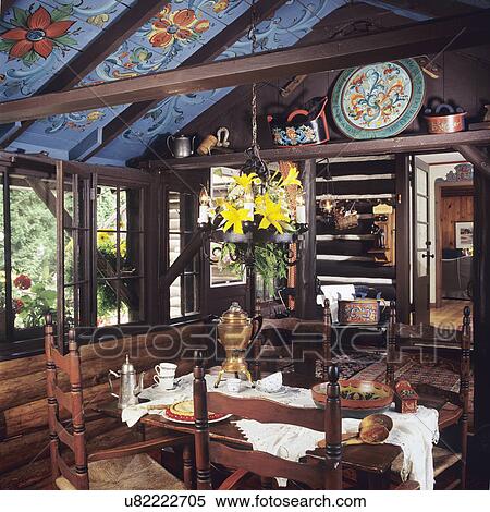DINING ROOM - Log walls, Norwegian Rosemaling floral painting on ceiling. Open door to hall, Accessories also Rosemaling, table set for coffee and dessert, dark beams and walls, yellow lilies in arrangement around chandelier. View Large Photo Image Stock Photography - DINING ROOM - Log walls, Norwegian Rosemaling floral painting on ceiling. Open door to hall, Accessories also Rosemaling, table set for coffee and dessert, dark beams and walls, yellow lilies in arrangement around chandelier. . Fotosearch
