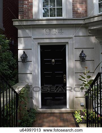 Stock Image - DOORS: EXTERIOR: city living, cut limestone with house numbers carved into stone, brick walkway, lanterns, step down from sidewalk, black railings on either side. Fotosearch