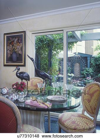 EATING AREA: Dining area, sliding doors looking outside, glass table with patterned dining chairs, metal egret bird sculptures, floral painting, plates and green stemmed glassware, teapots, yellow walls, detail View Large Photo Image Stock Photo - EATING AREA: Dining area, sliding doors looking outside, glass table with patterned dining chairs, metal egret bird sculptures, floral painting, plates and green stemmed glassware, teapots, yellow walls, detail . Fotosearch
