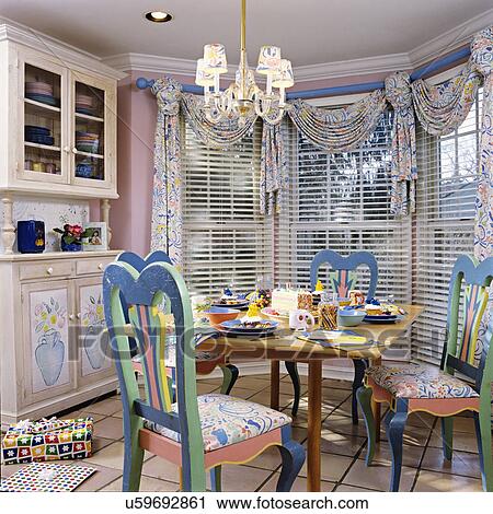 EATING AREA: Near kitchen. Pastel painted chairs, birthday party, table setting, chandelier, swag and jabot curtains with blinds, crown molding, display cupboard, tile floor. View Large Photo Image Stock Image - EATING AREA: Near kitchen. Pastel painted chairs, birthday party, table setting, chandelier, swag and jabot curtains with blinds, crown molding, display cupboard, tile floor.. Fotosearch