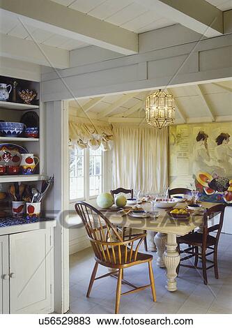 EATING AREAS: Cottage, exposed ceiling, beige and ivory mural painted on wall, partial view of kitchen shelves with colorful pottery balloon shades, mixed chair styles, 1800's oak table, 60's glass chandelier View Large Photo Image Stock Image - EATING AREAS: Cottage, exposed ceiling, beige and ivory mural painted on wall, partial view of kitchen shelves with colorful pottery balloon shades, mixed chair styles, 1800's oak table, 60's glass chandelier . Fotosearch